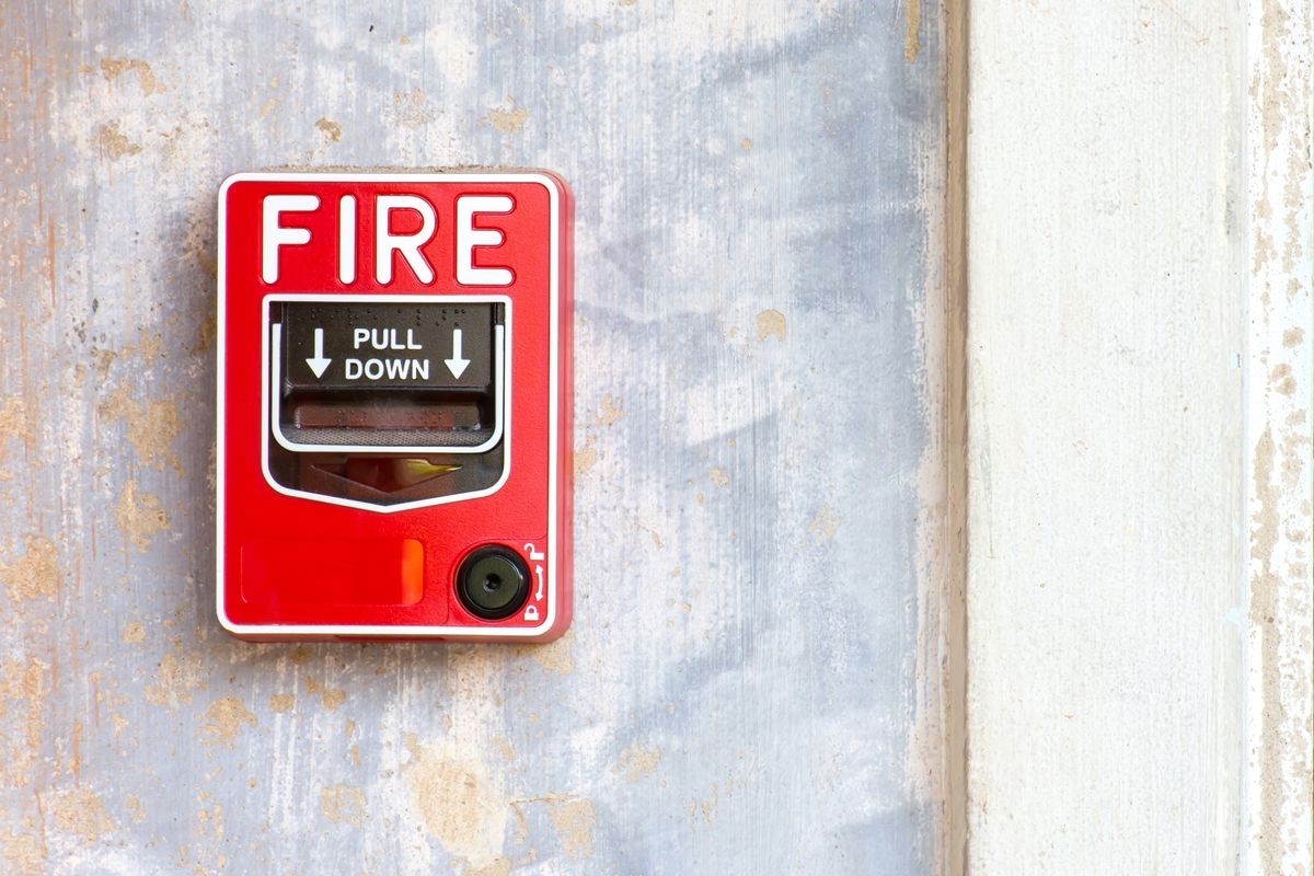 Red fire alarm box on white concrete wall background.
